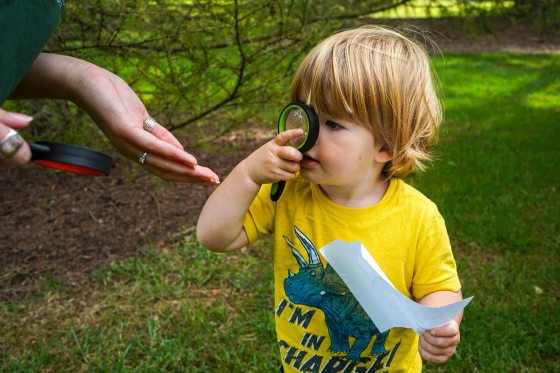 A small child looking through a black and green magnifying glass. 